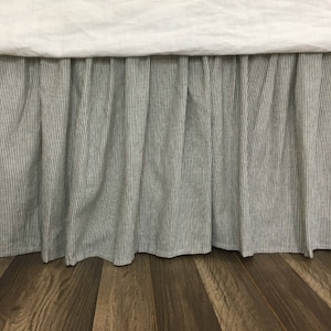 May include: A black and white striped bed skirt with a ruffled edge. The skirt is made of a linen fabric and is shown against a wood floor.