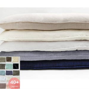 K&ouml;nnte beinhalten: Ein Stapel aus f&uuml;nf rechteckigen Kissen aus Leinen in verschiedenen Blaut&ouml;nen, Wei&szlig; und Beige. Die Kissen sind vom dunkelsten zum hellsten angeordnet, wobei das dunkelste blaue Kissen unten und das hellste beige Kissen oben liegt. Die Kissen bestehen alle aus einem weichen, nat&uuml;rlichen Leinenstoff. Der Text "40+ Choices" ist in der unteren rechten Ecke des Bildes sichtbar.