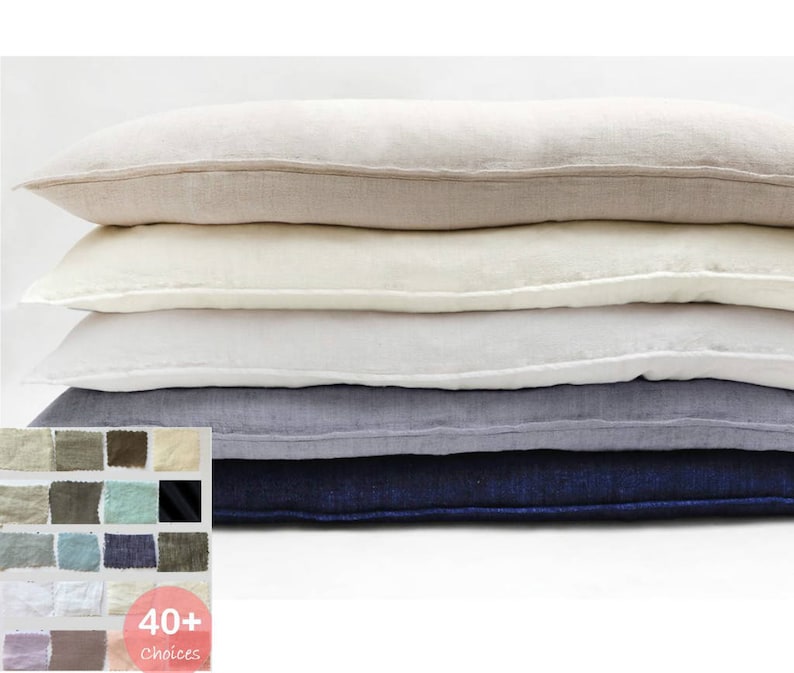 K&ouml;nnte beinhalten: Ein Stapel aus f&uuml;nf rechteckigen Kissen aus Leinen in verschiedenen Blaut&ouml;nen, Wei&szlig; und Beige. Die Kissen sind vom dunkelsten zum hellsten angeordnet, wobei das dunkelste blaue Kissen unten und das hellste beige Kissen oben liegt. Die Kissen bestehen alle aus einem weichen, nat&uuml;rlichen Leinenstoff. Der Text "40+ Choices" ist in der unteren rechten Ecke des Bildes sichtbar.