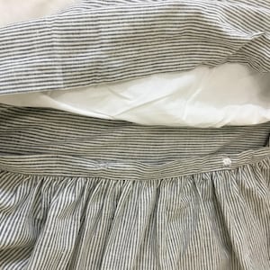May include: A white and blue striped bed skirt with a gathered ruffle. The skirt has a button closure.