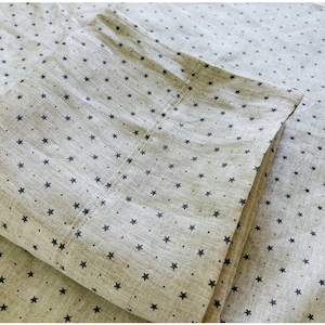 以下が含まれることがあります： 小さな黒い星柄のベージュの枕カバー2枚。枕カバーは折り畳んで重ねられています。