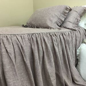 Puede incluir: Una falda de cama de lino malva con un borde con volantes. La falda está hecha de una tela suave y texturizada y tiene un aspecto relajado y casual.
