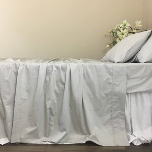 Pu&ograve; includere: Un letto bianco con un lenzuolo con angoli bianchi e un piumino bianco. Il letto &egrave; fatto con una gonna da letto bianca e ha un cuscino bianco con una federa bianca.
