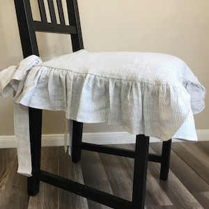 May include: A black wooden chair with a seat cushion cover. The cushion cover is white with blue vertical stripes and a ruffled edge. The cover is tied to the chair with fabric ties.