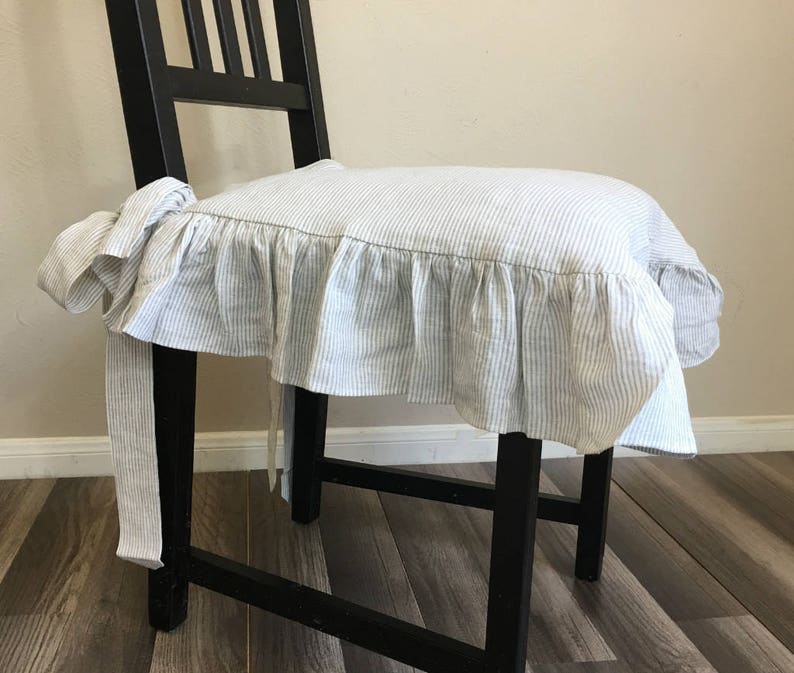 May include: A black wooden chair with a seat cushion cover. The cushion cover is white with blue vertical stripes and a ruffled edge. The cover is tied to the chair with fabric ties.