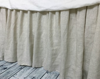 May include: A beige linen bed skirt with thin white stripes. The skirt is gathered and has a ruffled edge.