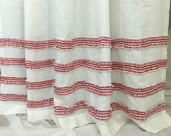Puede incluir: Cortina de lino blanco con volantes de rayas rojas y blancas. Los volantes están cosidos en filas horizontales a lo largo de la parte inferior de la cortina.