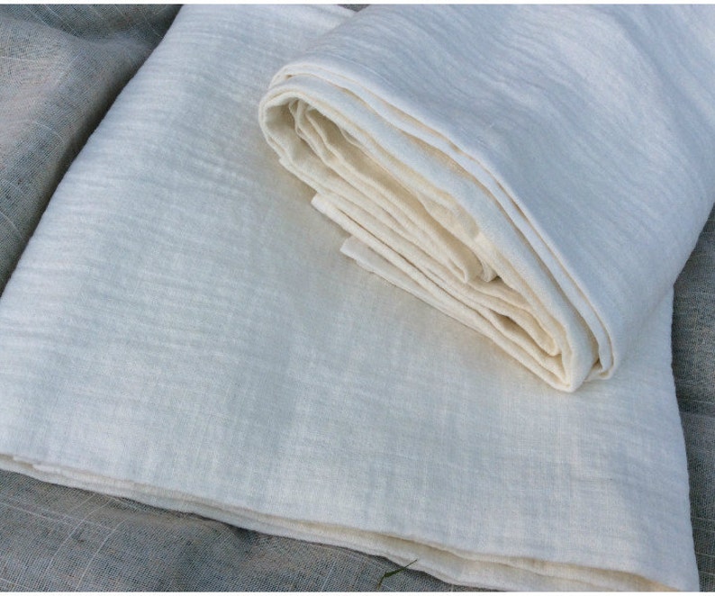Pu&ograve; includere: Due pezzi di tessuto di lino bianco, uno piegato e l'altro piatto. Il tessuto ha un aspetto morbido e testurizzato.