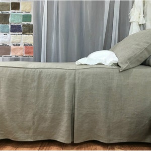 May include: A linen bed skirt in a light brown color with pleats along the bottom edge. The bed skirt is on a bed with white linen pillows and a white lace canopy.