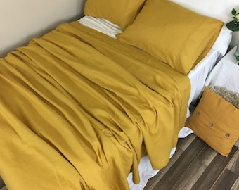 May include: A mustard yellow linen bedding set with a flat sheet, fitted sheet, and two pillowcases. The bedding is arranged on a bed with a white bed skirt.