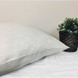 May include: A white linen pillow with a subtle textured surface. The pillow is lying on a white sheet.