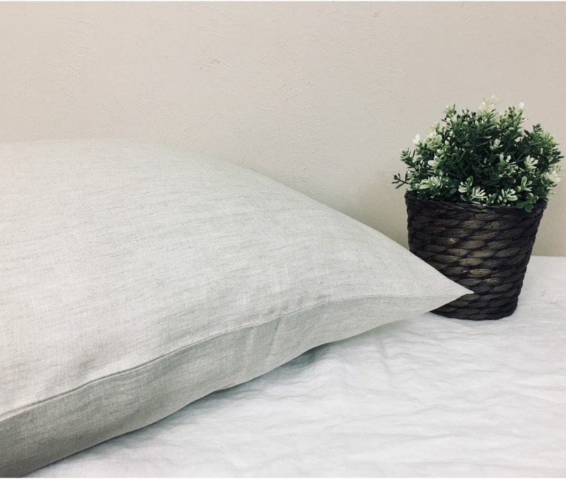 May include: A white linen pillow with a subtle textured surface. The pillow is lying on a white sheet.