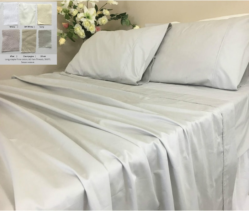 Pu&ograve; includere: Un letto grigio chiaro con un lenzuolo con angoli bianchi e due federe. Il letto &egrave; realizzato in cotone fine a fibra lunga, 600 fili, 300TC. L'immagine mostra un campione di tessuto in diversi colori: bianco, avorio, avorio, argento, champagne e ardesia.