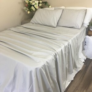 Pu&ograve; includere: Un letto grigio chiaro con un cuscino bianco e un cuscino bianco. Il letto &egrave; fatto con un lenzuolo grigio chiaro e una coperta grigio chiaro.