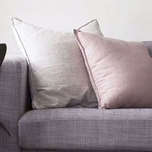 K&ouml;nnte beinhalten: Zwei Kissen auf einem lila Sofa. Ein Kissen ist wei&szlig; und das andere ist hellrosa.