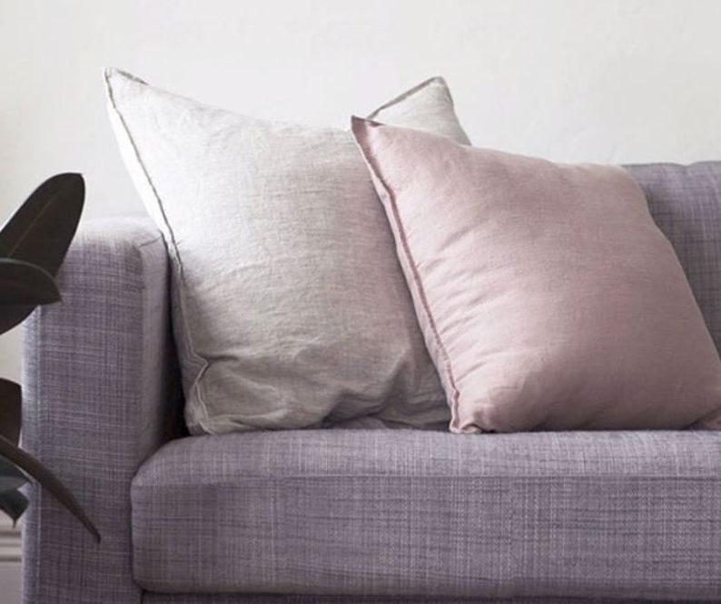 K&ouml;nnte beinhalten: Zwei Kissen auf einem lila Sofa. Ein Kissen ist wei&szlig; und das andere ist hellrosa.