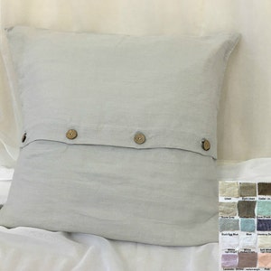May include: A light gray linen pillow with three wooden buttons. The pillow is on a white bedspread.