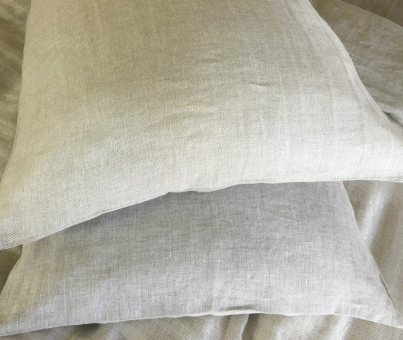 May include: Two light gray linen pillowcases stacked on top of each other. The pillowcases are made of a soft, natural fabric and have a subtle herringbone pattern.