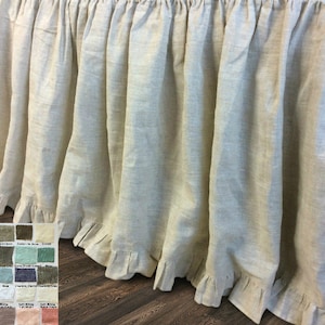 May include: A natural linen bed skirt with a ruffled edge. The skirt is a light beige color and is shown on a wooden floor.