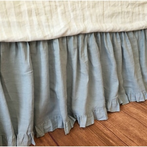 May include: A light blue bed skirt with a ruffled edge. The skirt is made of a soft, linen-like fabric.