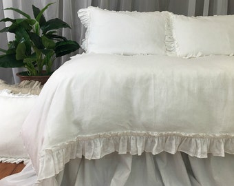 May include: White linen duvet cover with a ruffled edge. The duvet cover is on a bed with white ruffled pillowcases.