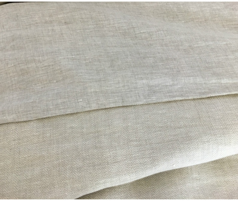 May include: Two pieces of beige linen fabric, one with a herringbone pattern and the other with a plain weave. The fabric is folded and the edges are visible.