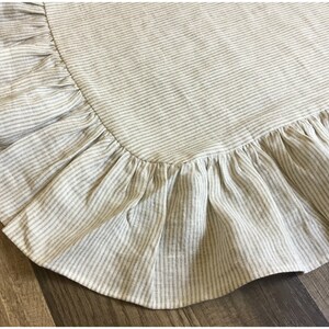 May include: Close-up of a beige and white striped fabric with a ruffled edge. The fabric has a textured appearance and is likely linen or a similar material. The ruffled edge adds a decorative element to the textile.