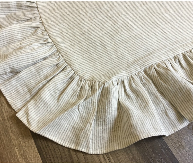 May include: Close-up of a beige and white striped fabric with a ruffled edge. The fabric has a textured appearance and is likely linen or a similar material. The ruffled edge adds a decorative element to the textile.