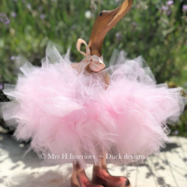 Powder pink tutu wearing, wooden duck, with rose gold boots and matching pink ribbon.