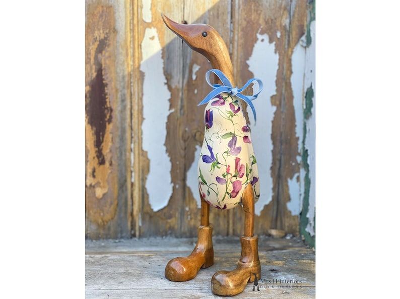 K&ouml;nnte beinhalten: Holzente Figur mit einem floral gemusterten Stoffk&ouml;rper und einer blauen Schleife. Die Ente hat Holzbeine und -f&uuml;&szlig;e.