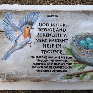 May include: A painted wooden sign featuring a bluebird in flight, a nest with blue eggs, and the text "PSALM 46 GOD IS OUR REFUGE AND STRENGTH, A VERY PRESENT HELP IN TROUBLE. THEREFORE WILL NOT WE FEAR THOUGH THE EARTH BE REMOVED, AND THOUGH THE MOUNTAINS BE CARRIED INTO THE MIDST OF THE SEA"