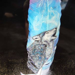 Puede incluir: Una pluma blanca con un dise&ntilde;o pintado en azul, morado y blanco de un lobo aullando a la luna. El lobo est&aacute; pintado en tonos de gris y blanco.