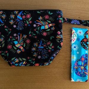 Puede incluir: Una bolsa negra con cremallera con un estampado colorido de colibríes y flores. Viene con una correa de tela azul y blanca a juego con un estampado floral.