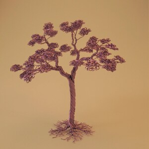 May include: A handcrafted copper wire tree sculpture. The tree features a twisted trunk, delicate branches, and textured foliage. The roots are also made of copper wire. The sculpture is a unique decorative item.