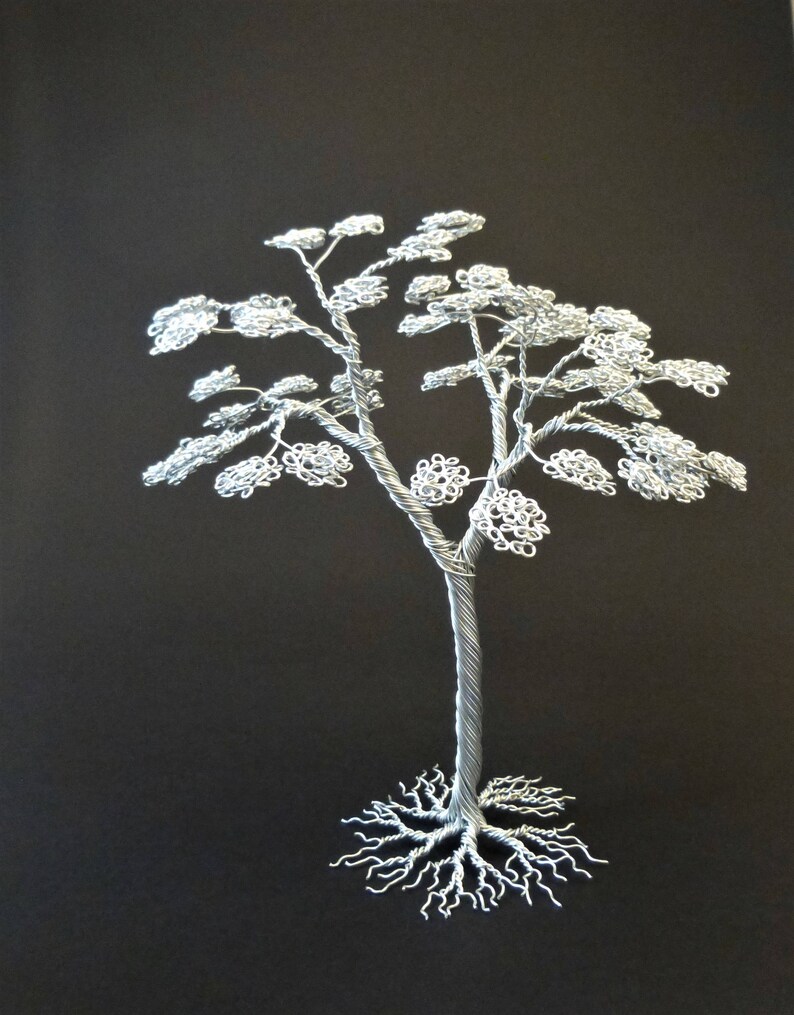 May include: A handcrafted silver wire tree sculpture against a black background. The tree features a detailed trunk, branches, and delicate, textured leaves. The roots are also intricately designed. This unique piece of art is a decorative item.