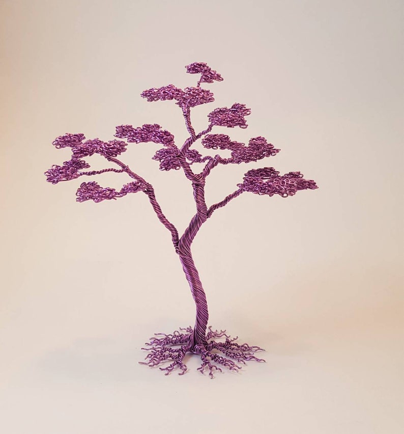 May include: A handcrafted, decorative wire tree sculpture in a vibrant purple hue. The tree features a twisted trunk, delicate branches, and a full crown of leaves, with intricate root details at the base. This unique piece is a decorative accent.