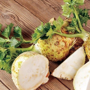 Könnte beinhalten: Eine Nahaufnahme von Sellerieknolle, auch bekannt als Knollensellerie, wobei ein Teil der Knolle halbiert ist. Die Sellerieknolle ist hellgelb und hat eine raue Textur. Die Sellerieknolle ist von grünen Sellerieblättern umgeben.