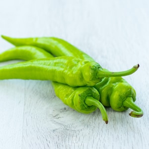 Op de afbeelding: Drie groene pepers, gestapeld op een wit houten oppervlak.