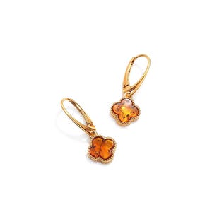 Peut inclure: Une paire de boucles d'oreilles à levier dorées. Chaque boucle d'oreille présente un motif de trèfle à quatre feuilles avec un centre de couleur ambre chaud et une bordure dorée décorative. Les boucles d'oreilles sont présentées sur fond blanc.