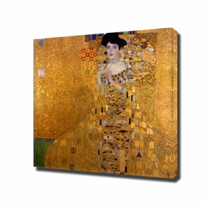 Op de afbeelding: Een canvas print van een portret met een vrouw in een gouden jurk en zwarte hoed. Het kunstwerk heeft een gouden achtergrond met ingewikkelde patronen en details. De vrouw draagt een choker en armbanden.