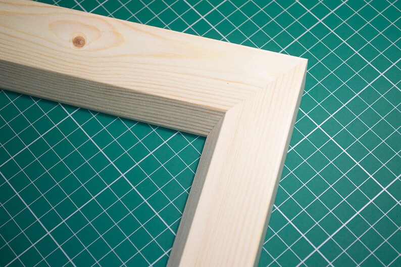 May include: Close-up of a corner of a natural wood picture frame. The frame is made of unfinished pine wood and has a simple, rectangular shape.