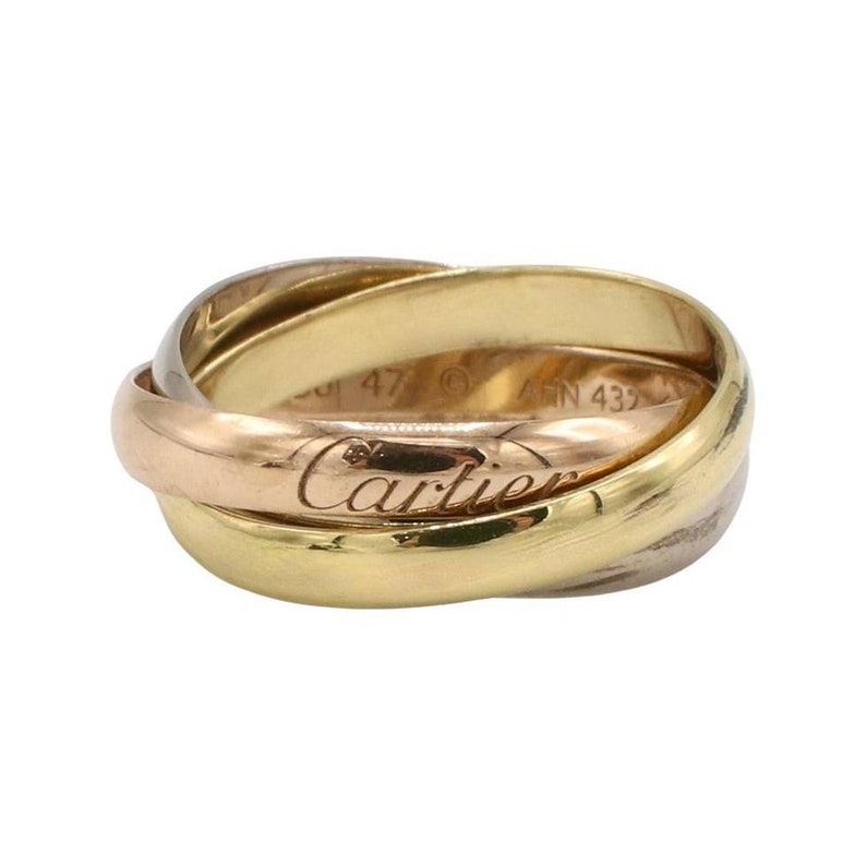 May include: A gold, silver, and rose gold Cartier Trinity ring. The ring has three bands that are intertwined. The inscription 'Cartier' is engraved on the rose gold band. The ring is size 47.
