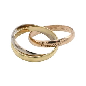 May include: A gold, silver, and rose gold interlocking ring set with the word 'Cartier' engraved on the band. The ring is marked 'A7 AHN 432'.