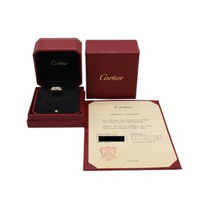 May include: A red Cartier box with a white Cartier ring inside. The ring is made of gold and has a diamond in the center. The box is open and the ring is visible. There is a certificate of authenticity for the ring with the text 'Cartier CERTIFICATE / CERTIFICAT' and 'En or 18 carats or en platine, nous certifions que ce bijou est un Cartier authentique.' and 'Made in 18k gold or platinum, we certify that this is an authentic Cartier jewel.' and '11-20-17' and '1535138'.