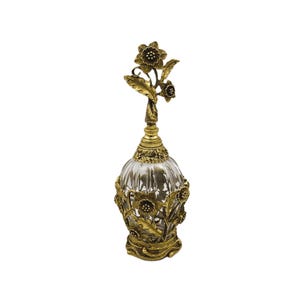 May include: A gold-toned glass perfume bottle with a floral design. The bottle has a clear glass body with a textured surface and a gold-toned metal cap with a floral design.