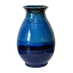 May include: A handcrafted ceramic vase with a glossy finish. The vase features a gradient of blues, transitioning from a deep navy at the base to lighter shades towards the top. The rim has a darker, textured appearance.