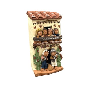 May include: A ceramic figurine of a multi-story house with people on the balcony and two people playing music in front. The house is painted in shades of brown, white, and green.