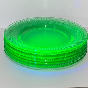May include: A stack of four circular plates made of translucent, vibrant green glass. Each plate features a distinct, radiating swirl pattern etched into the rim, creating a textured effect that contrasts with the smooth, flat center of the plates.