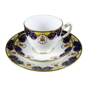 May include: A white teacup and saucer set with a blue and gold floral pattern. The cup has a delicate handle and the saucer has a scalloped edge.