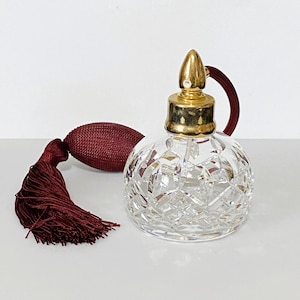 May include: A clear, cut-glass perfume bottle with a gold-colored top and a burgundy atomizer bulb and tassel. The round bottle has a diamond-cut pattern. The atomizer bulb and tassel are a deep burgundy color.